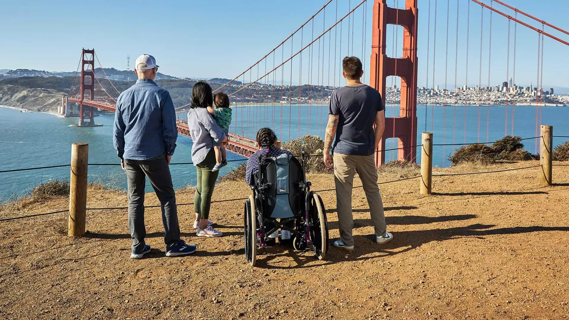 一群人, 包括一个坐轮椅的人, is seen from behind as they look at the 金门大桥 from the Marin Headlands.