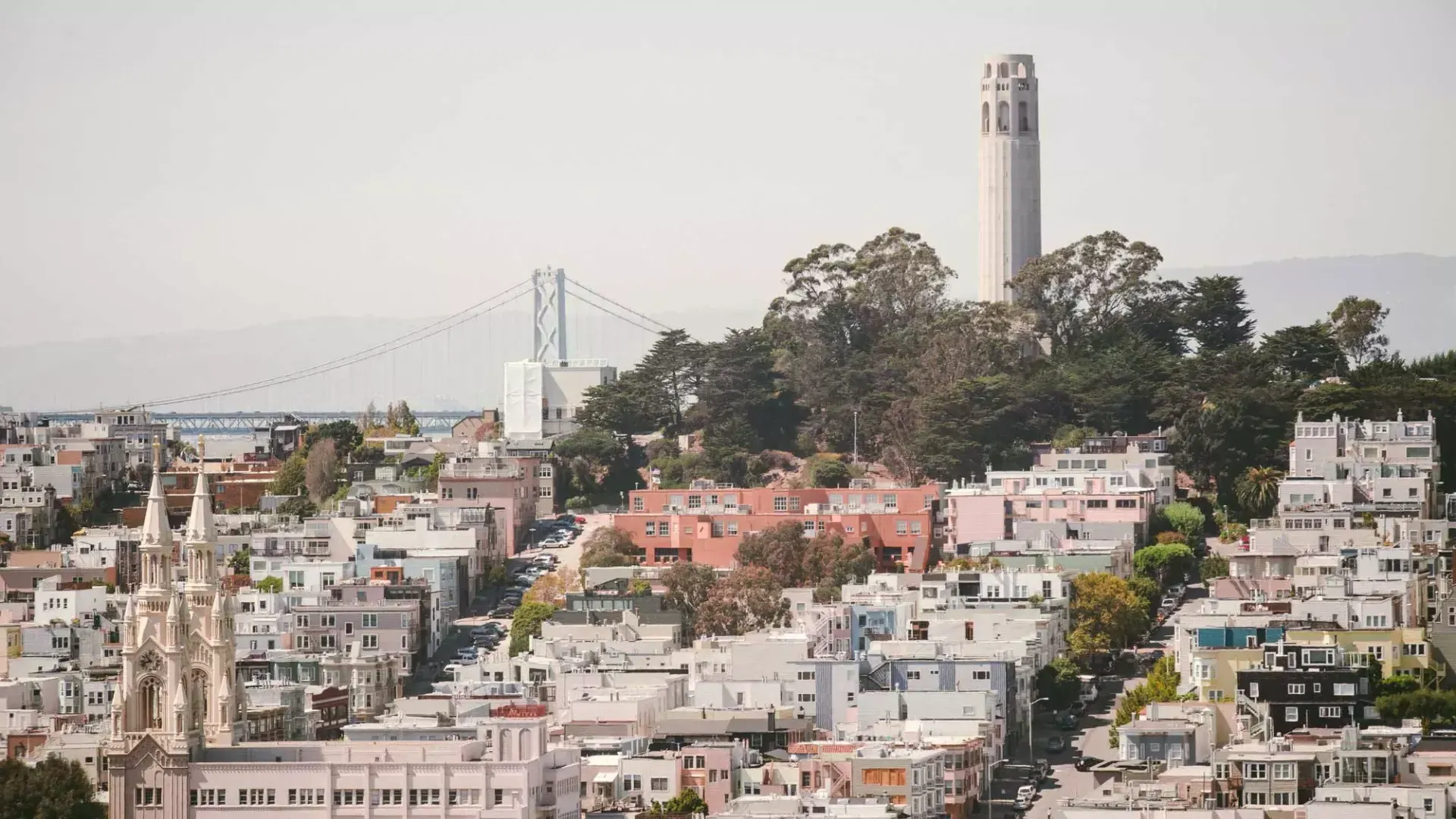 贝博体彩app的科伊特塔(Coit Tower)以海湾大桥(Bay Bridge)为背景，前景是一座覆盖着房屋的小山。.