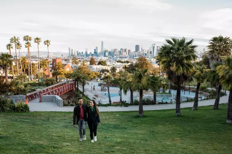 Una pareja camina hacia la cámara con Dolores Park y el Skyline de 贝博体彩app detrás de ellos.