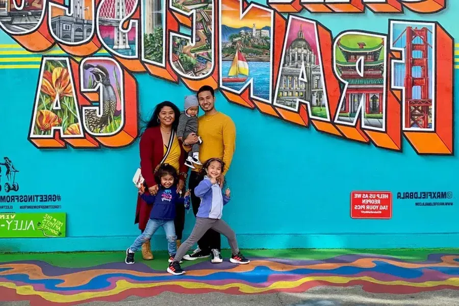 A family posing for A photo in front of A San Francisco mural