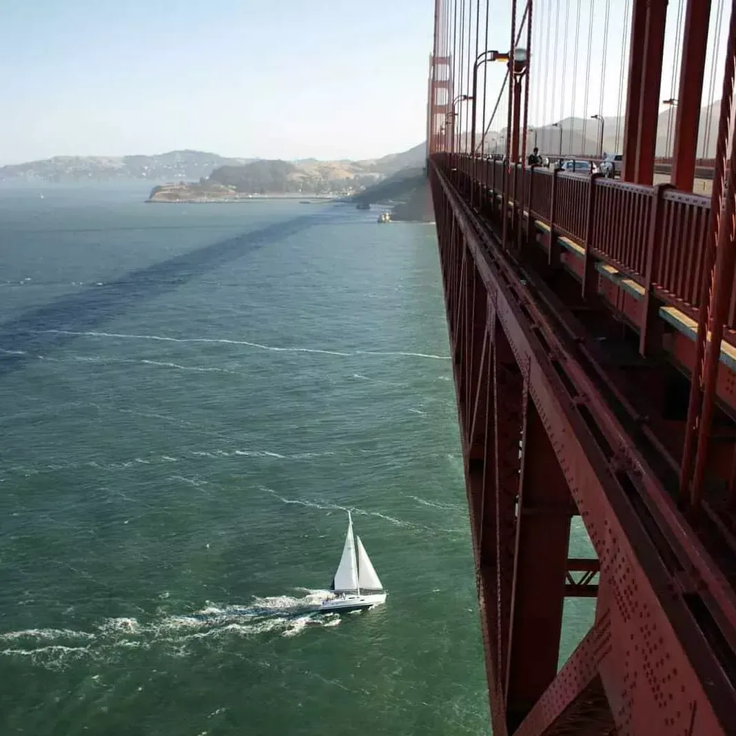 A small sailboat passes beneath the 金门大桥 in the San Francisco Bay.